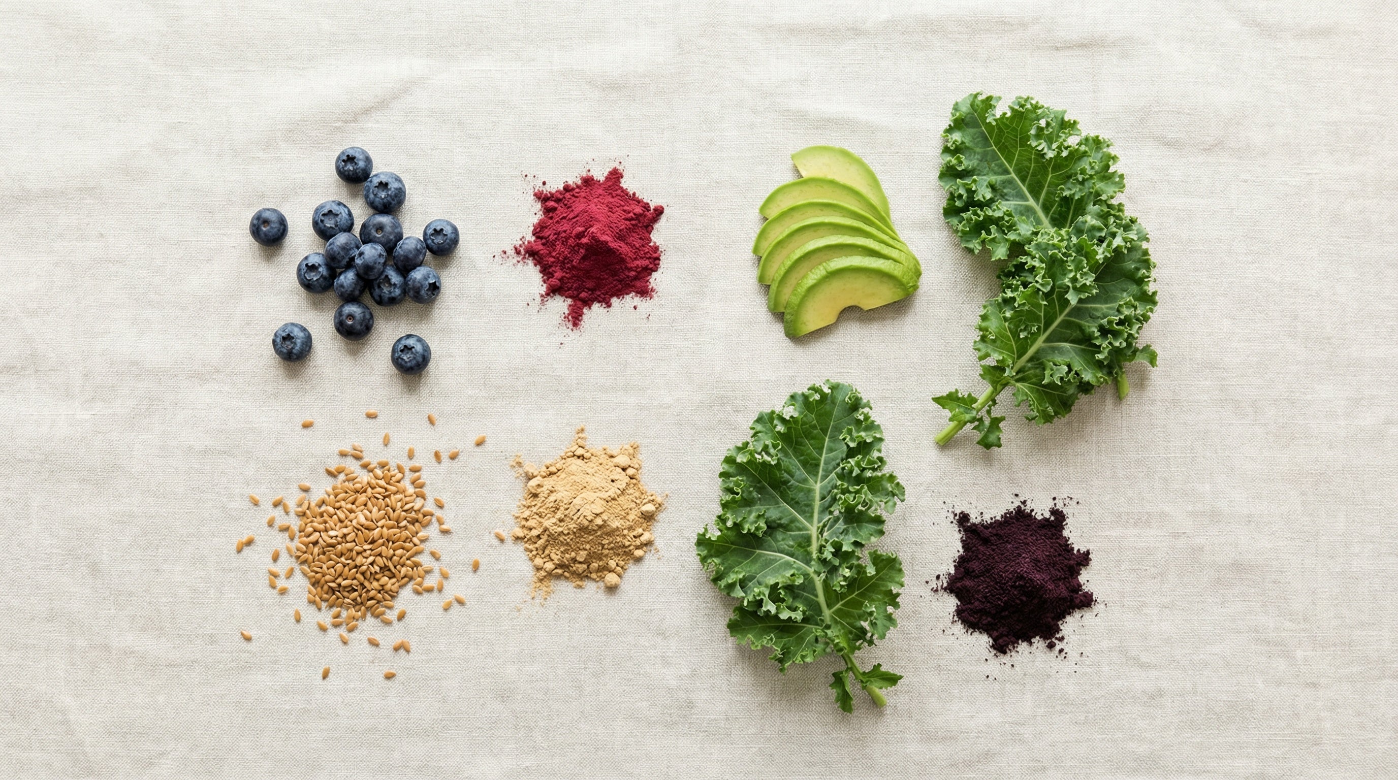 Flat lay product photography blueberries, flax seeds, beetroot powder, maca powder, acai powder, sliced avocado, kale leaves. 